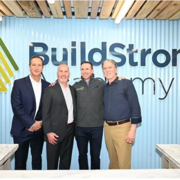 Employees smiling in front of a Build Strong Academy sign.