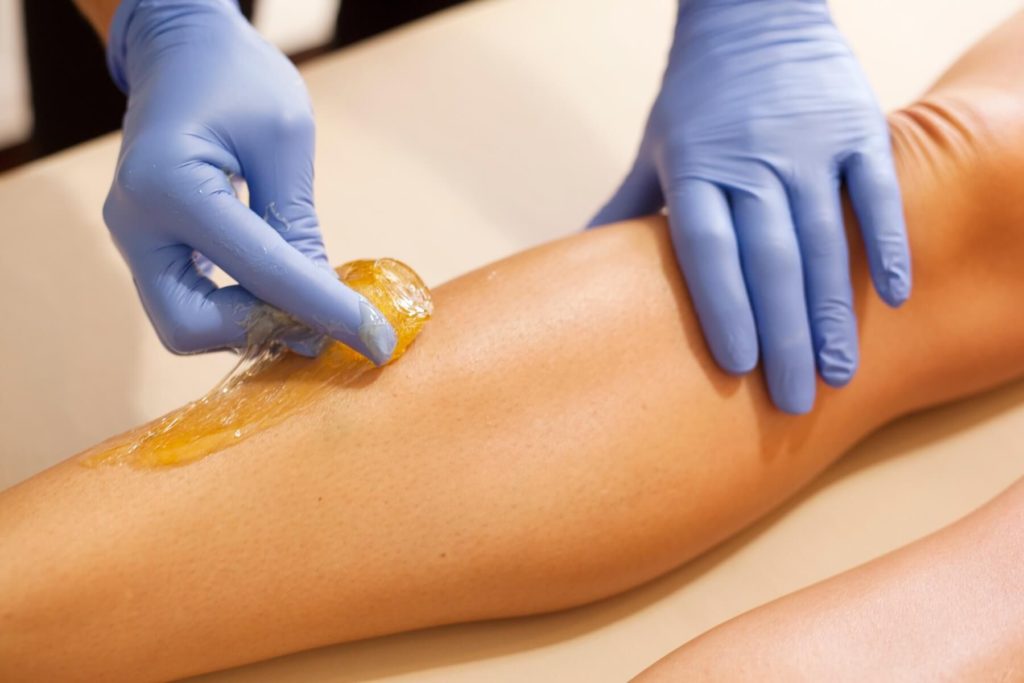 A ball of sugar being applicated to someone's leg. The person applying the sugar is wearing blue latex gloves.