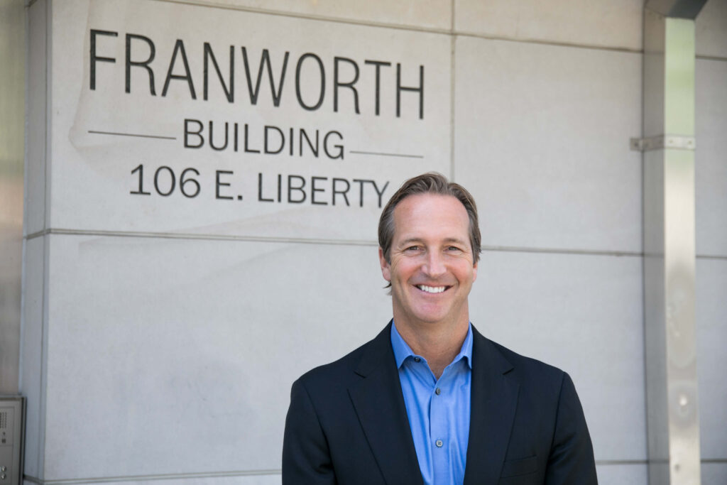 John Rotche in a suit standing outside the Franworth building smiling. Scale your business with Franworth.