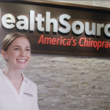 Receptionist smiling at a customer in front of a HealthSource sign.