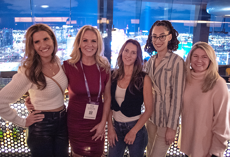 A group of female franchise professionals standing next to each other smiling, with glass walls behind them overlooking Las Vegas