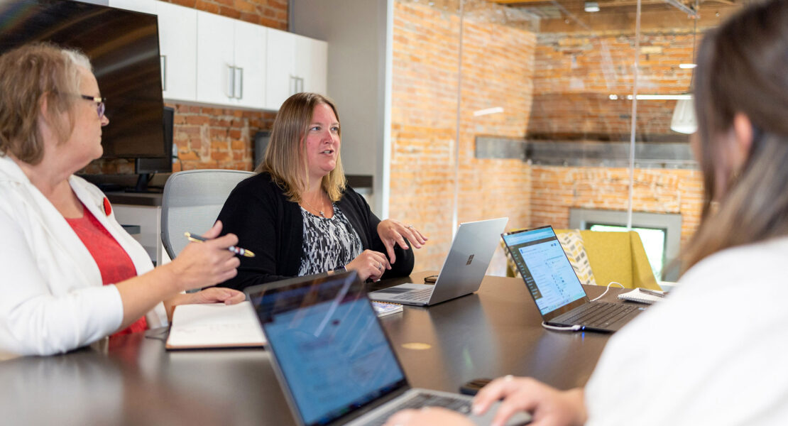 Three women sitting around a table with laptops.