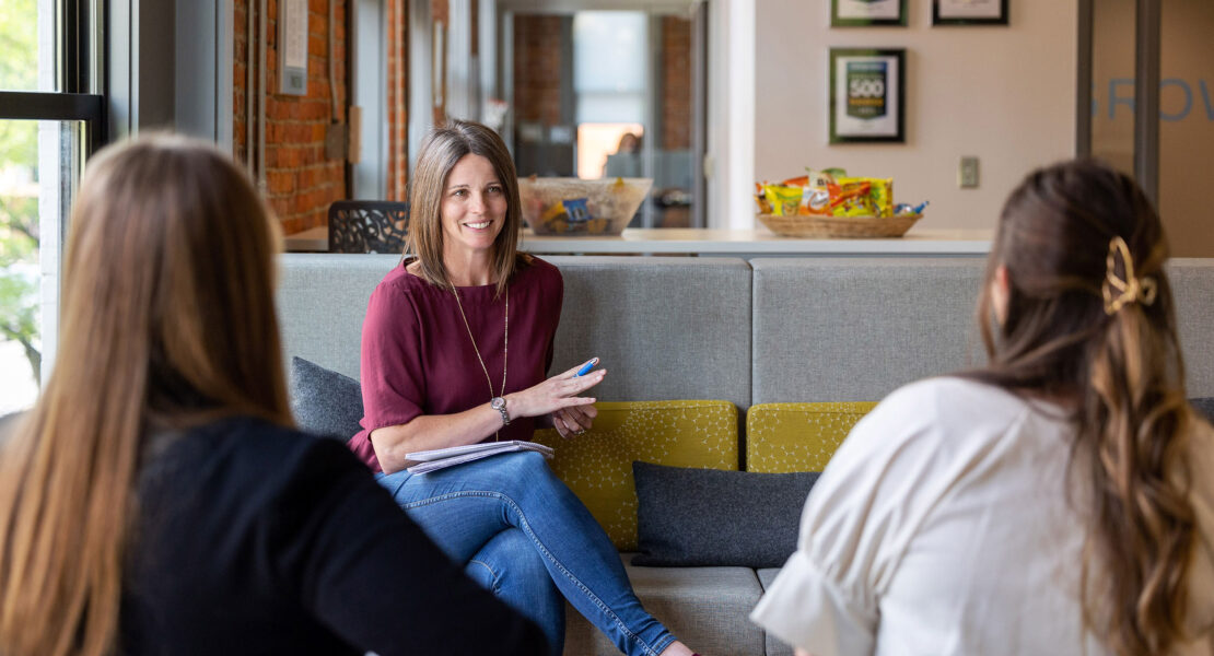 A business woman discussing how franchises work to two other women on a couch.