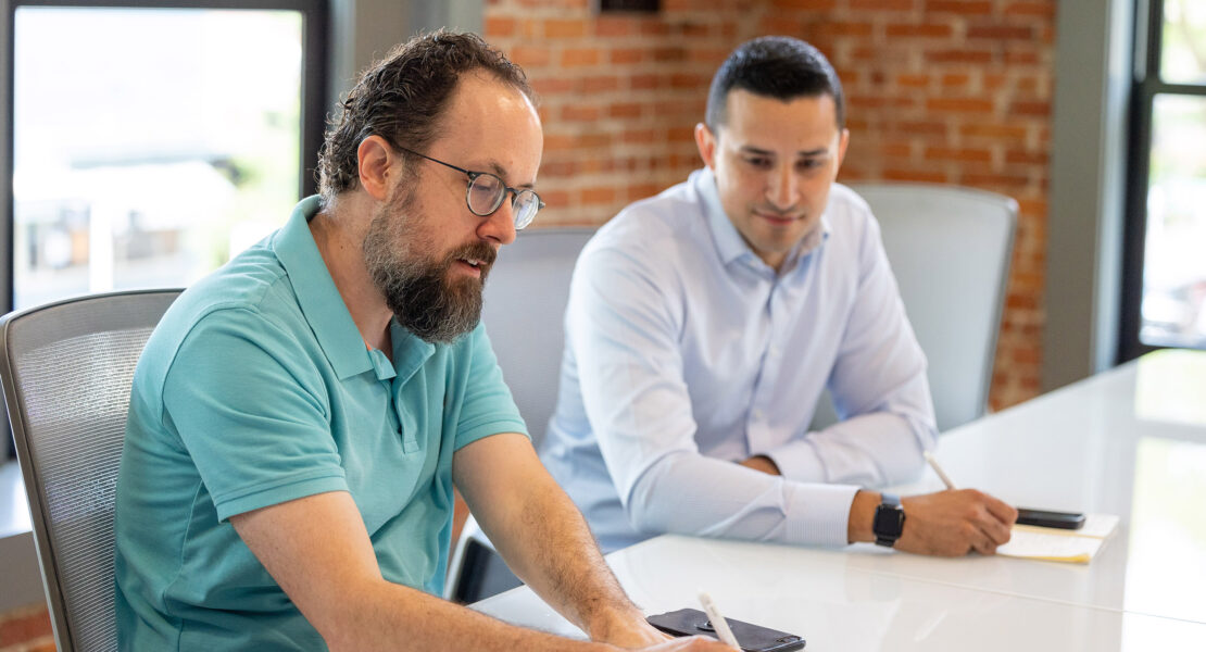 Two men discussing the advantages of franchising while writing on a piece of paper at a table.